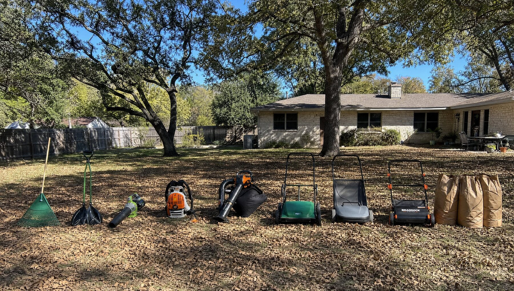 Nine leaf cleanup tools spread across a suburban yard, with a large pile of live oak leaves waiting to be tested.